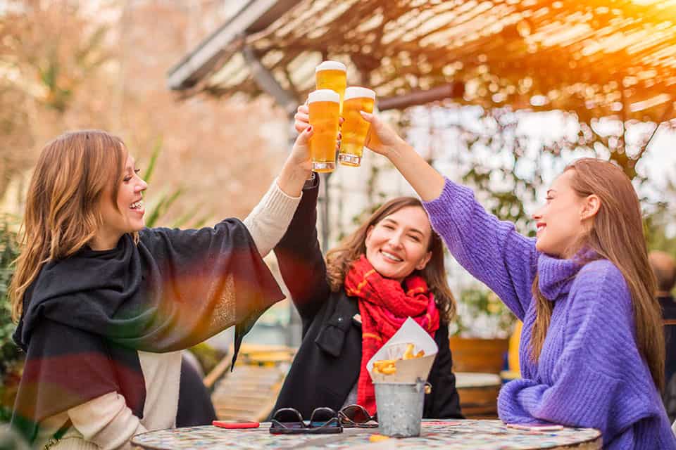 Group of women best friends clinking glasses of beer in restaurant - female friendship and having fun concept